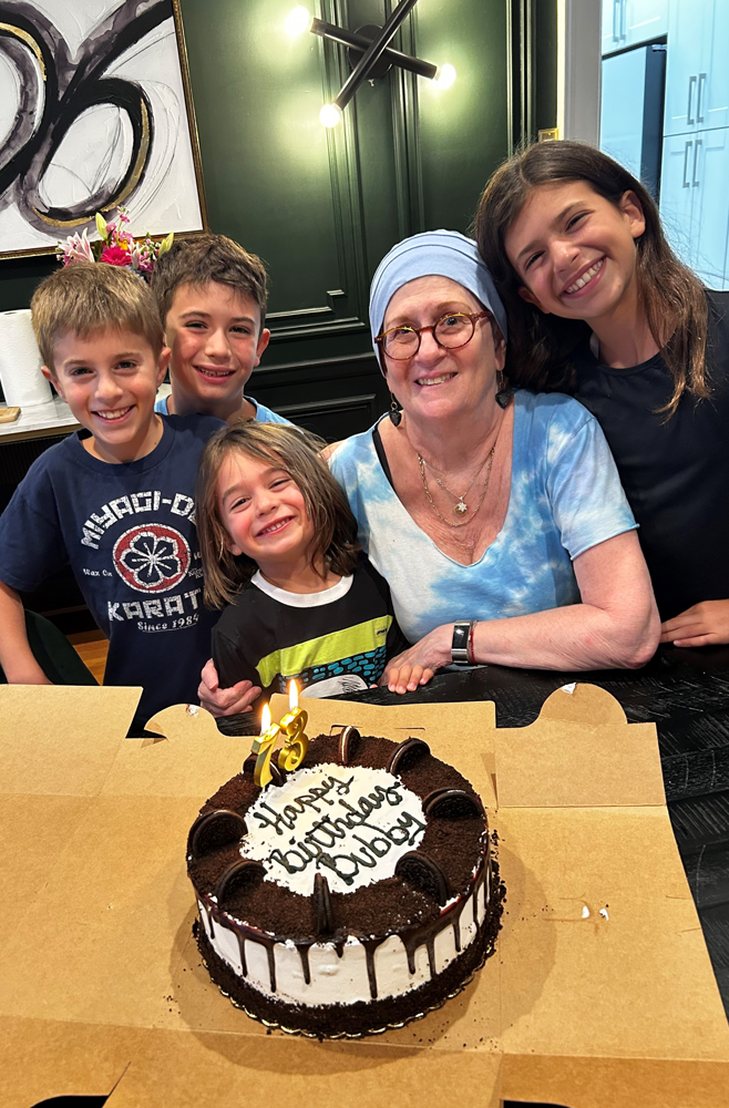 Glioblastoma patient Lynn Oxenberg smiles with her grandchildren and 73rd birthday cake that reads, "Happy Birthday Bubby"